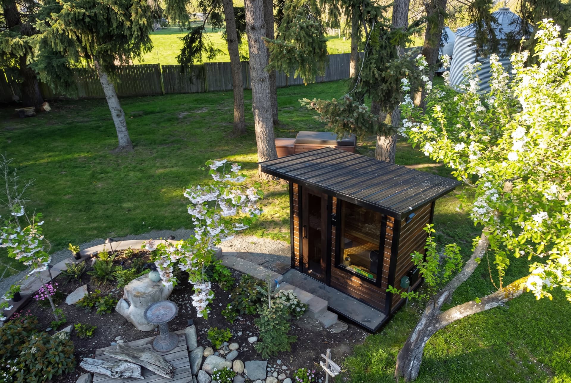 Cedar sauna with a standing-seam roof and glass front, viewed from above in the garden