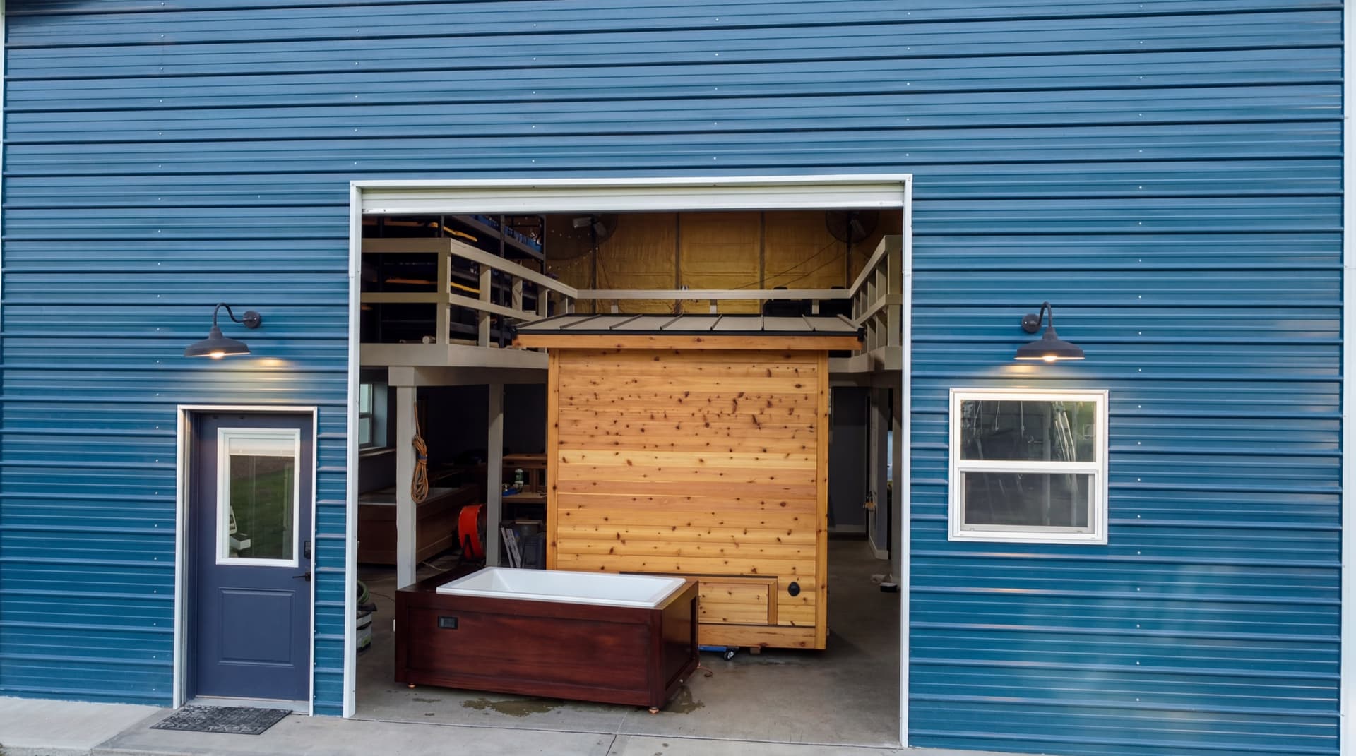 The Yutori shop in Graham, WA — roll-up door open at dusk, a cedar sauna and mahogany cold plunge staged in the bay