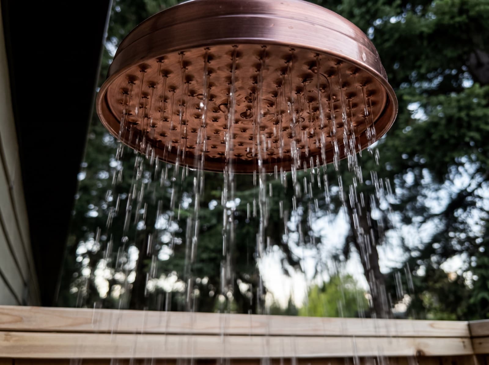 Close-up copper rain head with water falling over cedar outdoor shower
