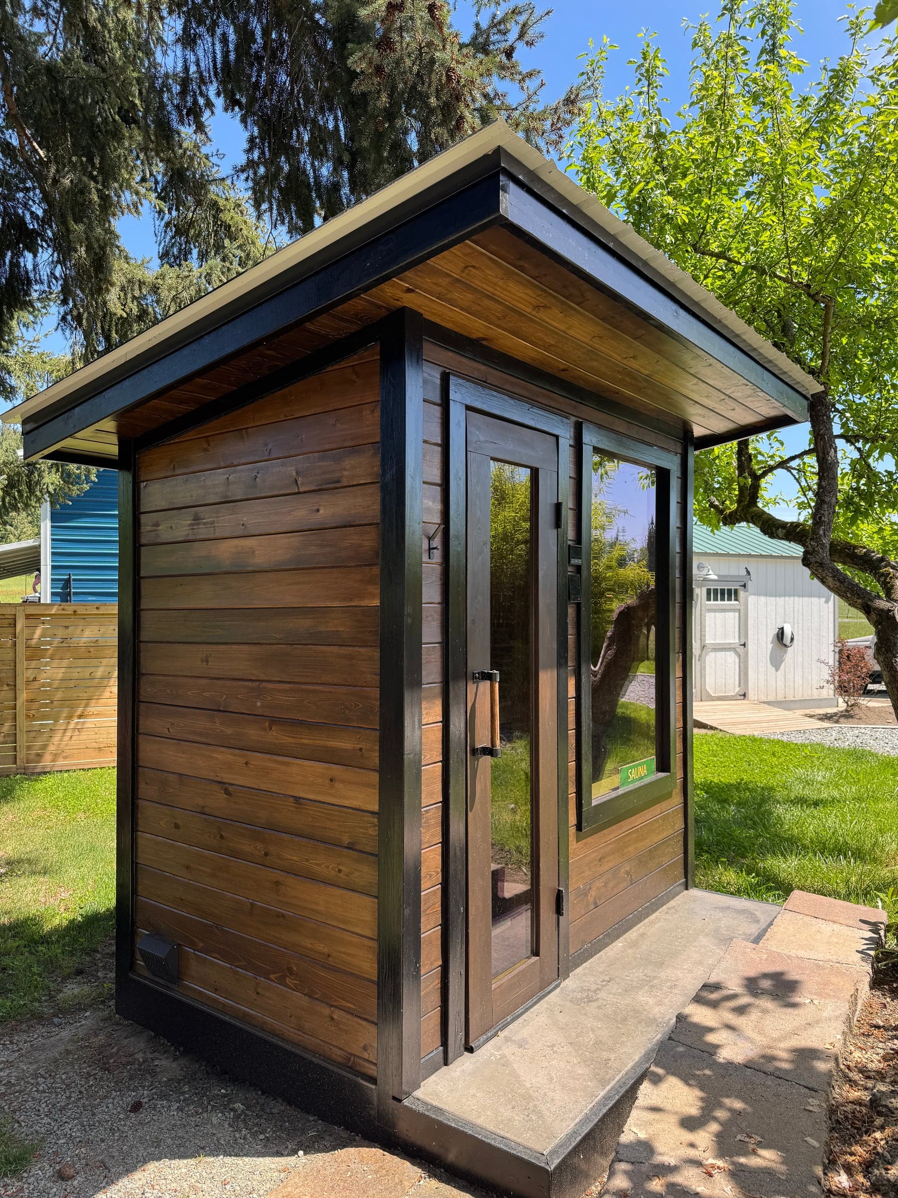 Complete cedar sauna in daylight, with the roof, side cladding, glass door, and front step visible