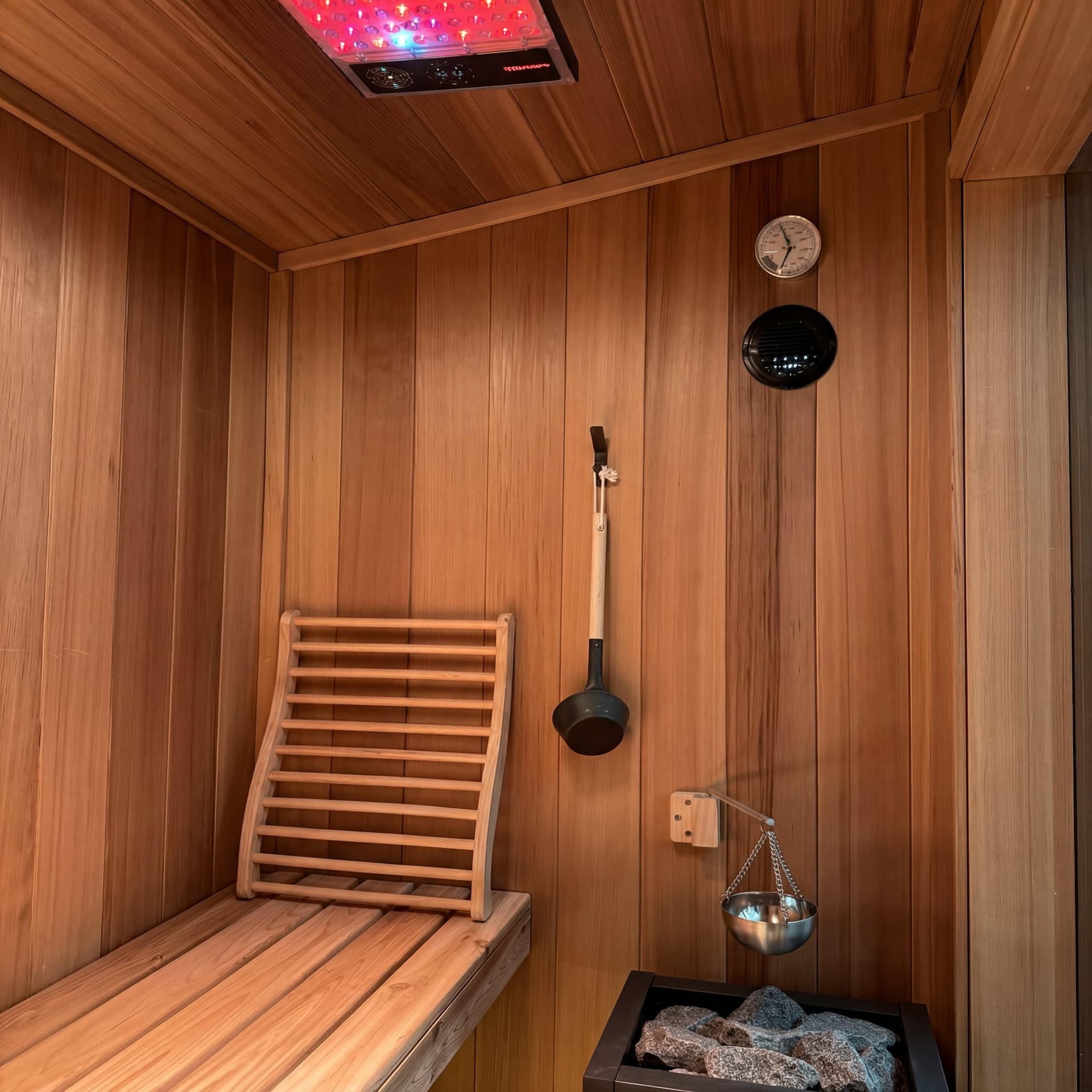 Cedar hot room with bench, backrest, ladle, stone heater, and an optional overhead light panel