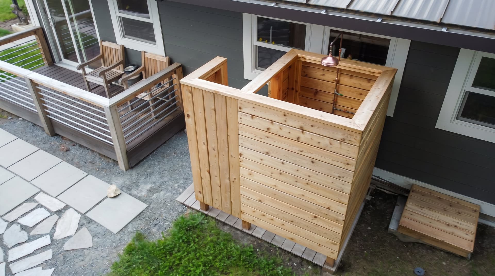 Complete cedar outdoor shower enclosure beside the deck, with the copper rain head visible inside