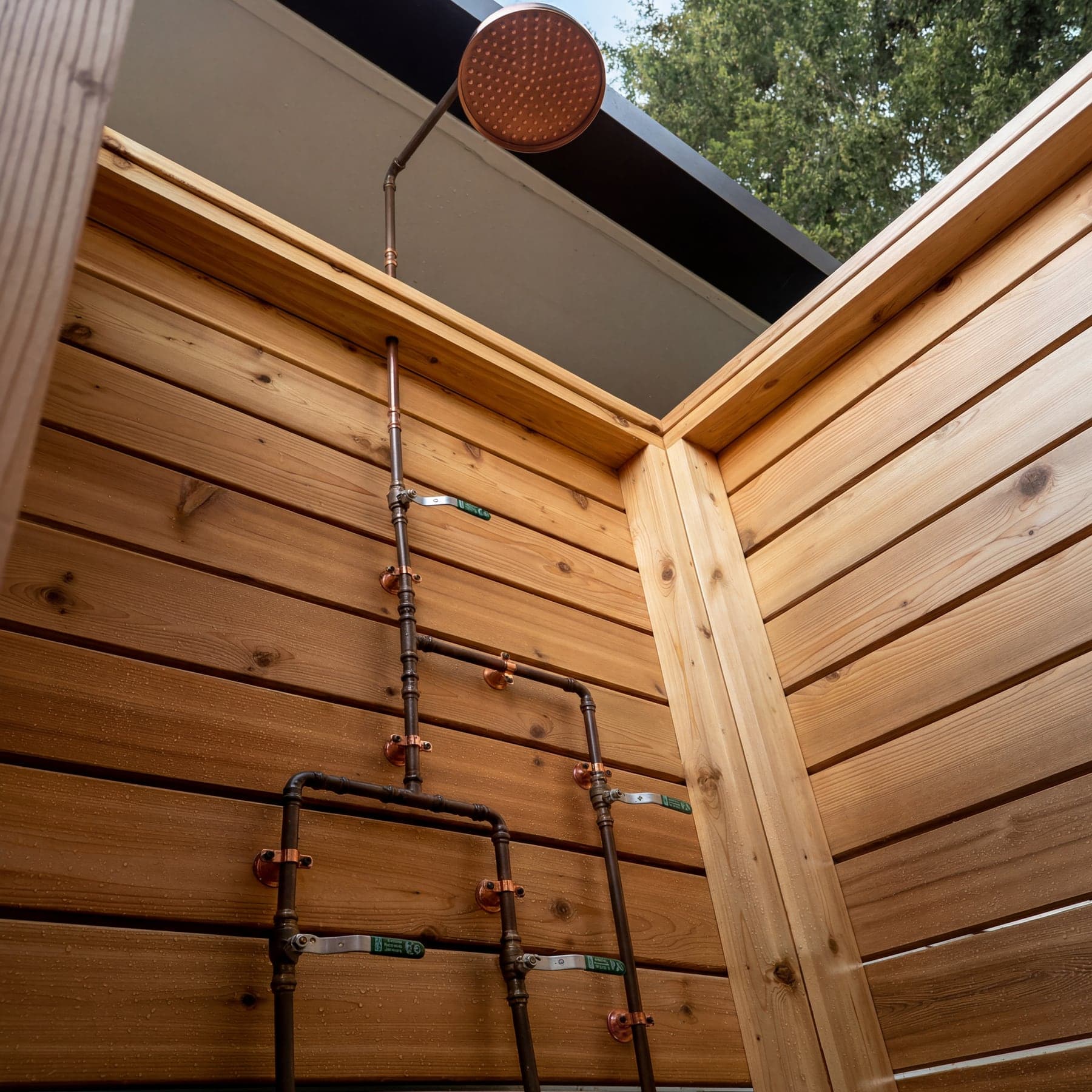 Copper rain head, riser, and exposed valves against the cedar shower walls